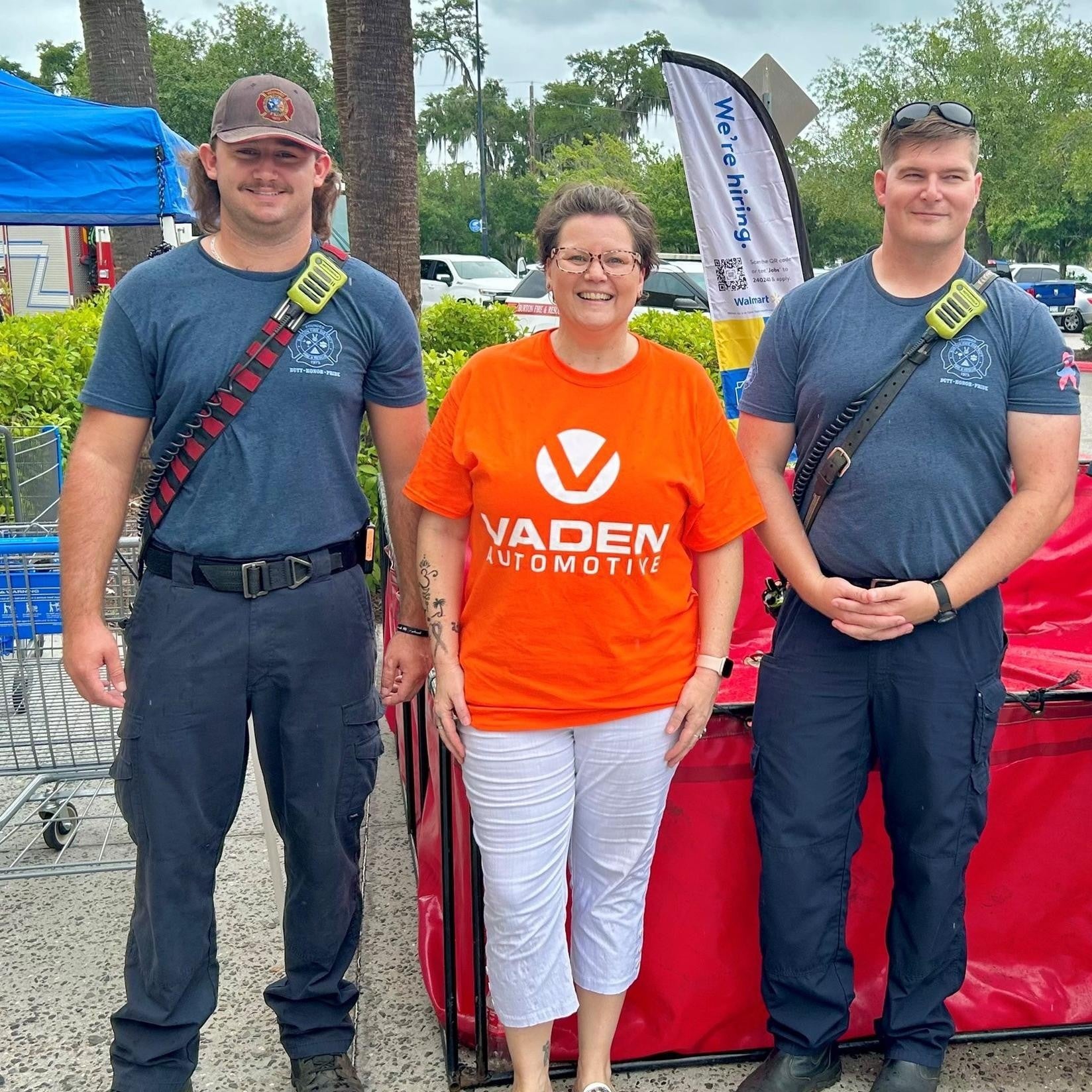 Two firefighters with someone in a bright orange Vaden Automotive shirt in between them.