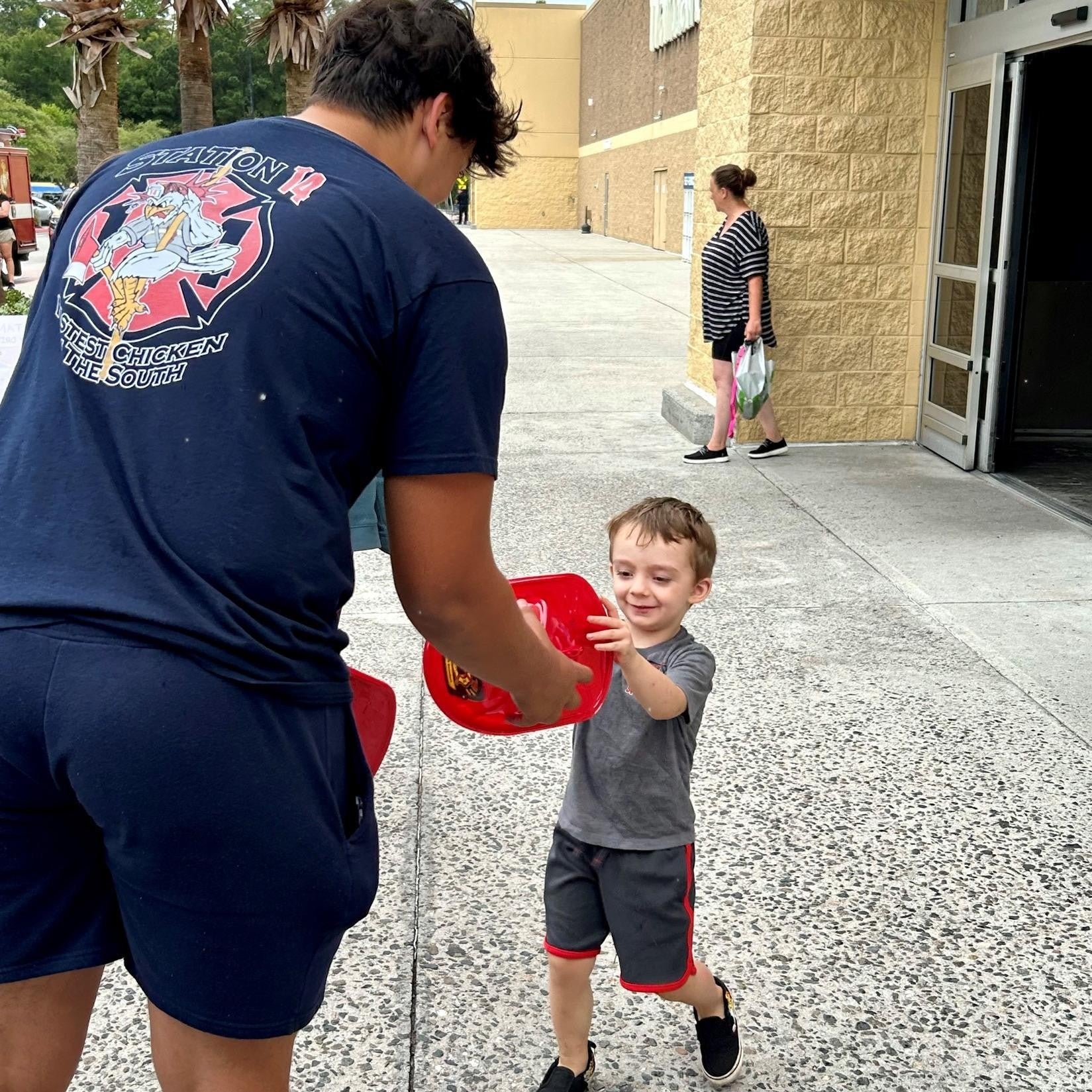 A firefighter giving a child a plastic firefighter hat.